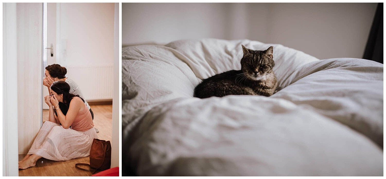 Zwei Frauen lächeln gespannt durch eine Tür, während die Katze im hellen Zimmer ruht – Hochzeitsreportage NRW.