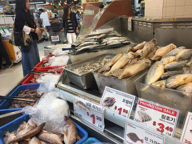 The supply of imported agro-fishery foods from South Korea is expected to exceed a total cost of $1 billion this year. A customer is tasting kimchi at a Korean market.