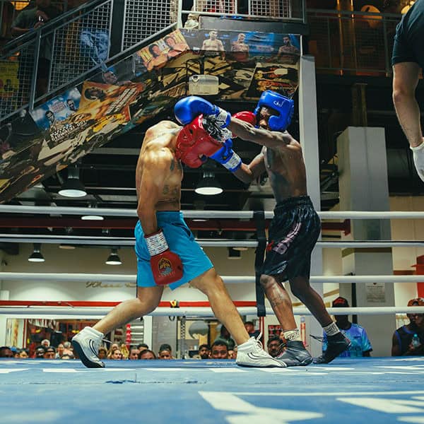 In our Dubai gym’s ring, elite fighters in blue and black shorts trade punches as the referee and an engaged crowd observe closely.