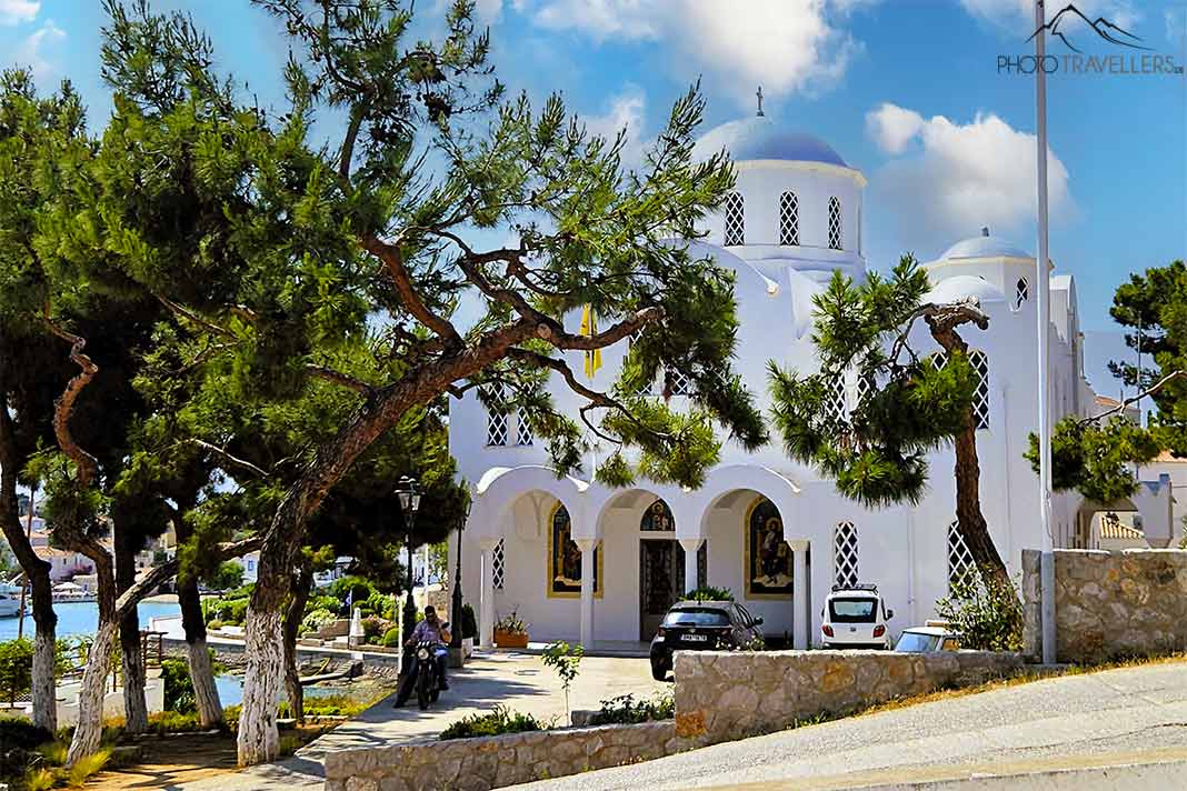 Die weiße Kirche Agios Nikolaos besticht mit blauer Kuppel und Bäumen im Vorgarten