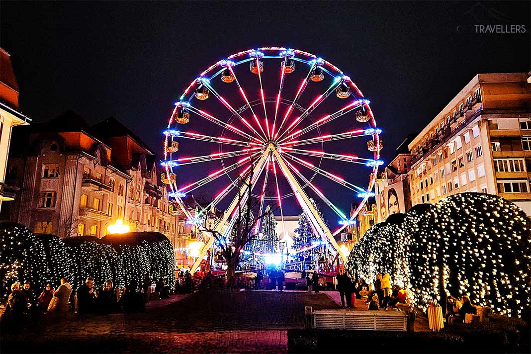Ein beleuchtetes Riesenrad steht zwischen den beleuchteten Fassaden der Piata Victoriei