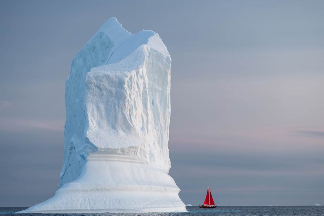 Ein rotes Segelboot vor einem Eisberg am Ilulissat-Eisfjord in Grönland