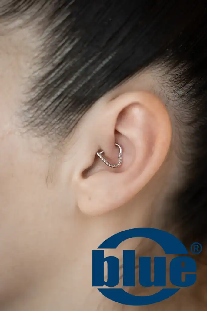 Close-up of a silver twisted hoop earring worn in the ear lobe on a person with dark hair. Potential logo partially visible at bottom right.