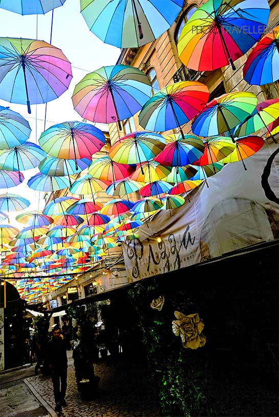 Viele bunte Regenschirme hängen zwischen den Häuserzeilen einer schmalen Passage