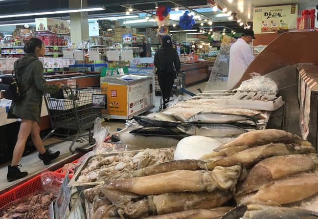 Zion Market’s seafood department employee is organizing the displayed squids amid its soaring prices, while beef prices are decreasing.