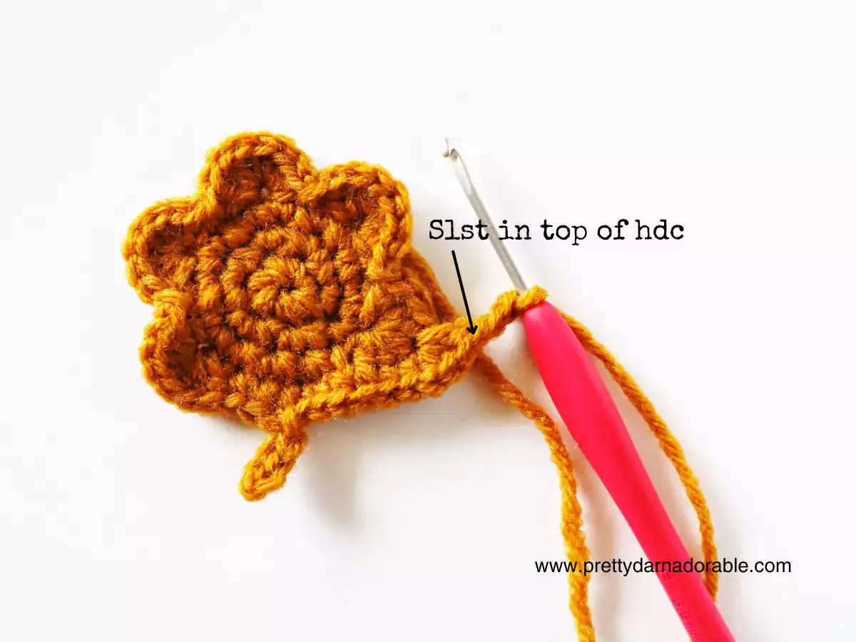 A pink-handled crochet hook is in a rust maple leaf motif; arrow marks where to slip stitch. www.prettydarnadorable.com at bottom right. Free crochet pattern