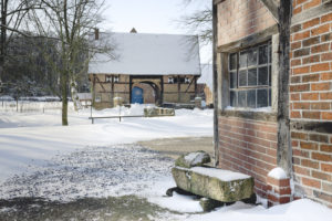 Hochzeitslocation Haus Runde 8 Schneebedeckter Innenhof in Münster mit Backsteingebäuden, kahlen Bäumen und einer blauen Tür im Hintergrund.