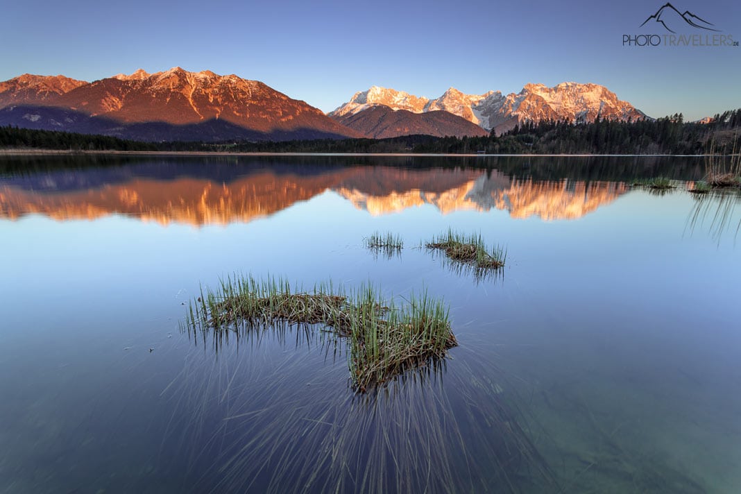 Der Blick über einen Bergsee am Abend, im Hintergrund angestrahlte Berge