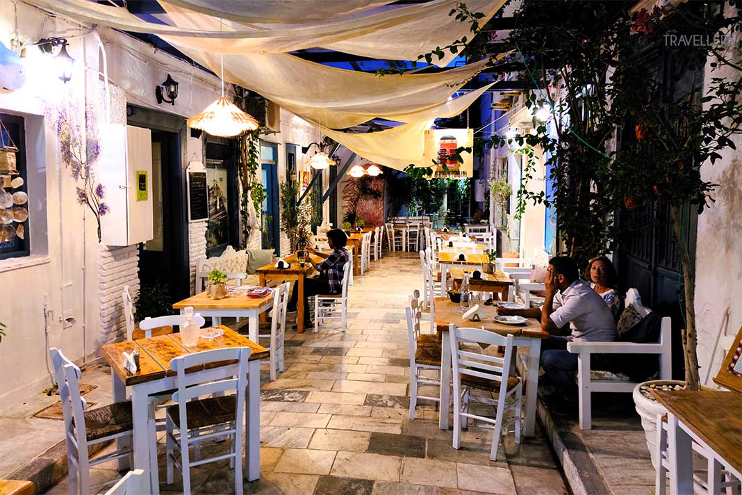 An den Tischen und Stühlen einer Taverne in einer Gasse sitzen wenige Menschen