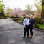 A man riding a skateboard down a sidewalk in front of a house