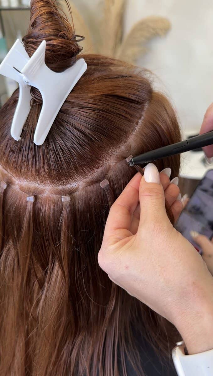 Hair extensions being fitted in a row along the parting on auburn hair