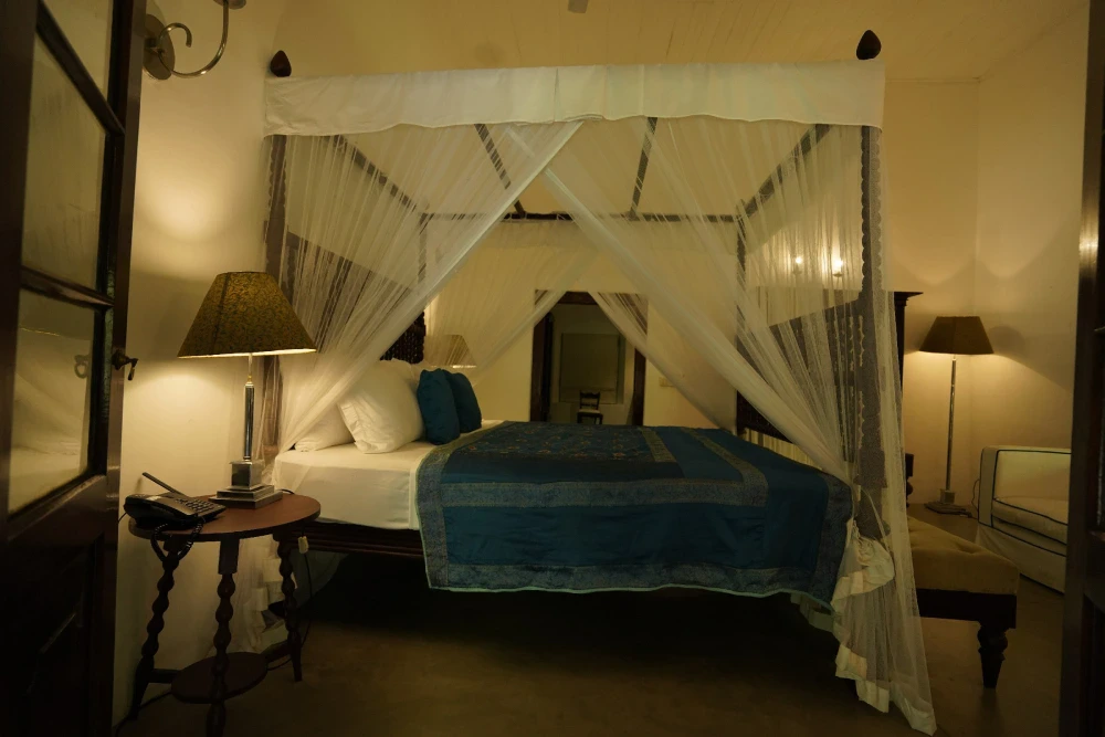 A luxurious bed with a canopy in the Peacock Royal room of Adigar's manor, showcasing elegant decor and rich fabrics.