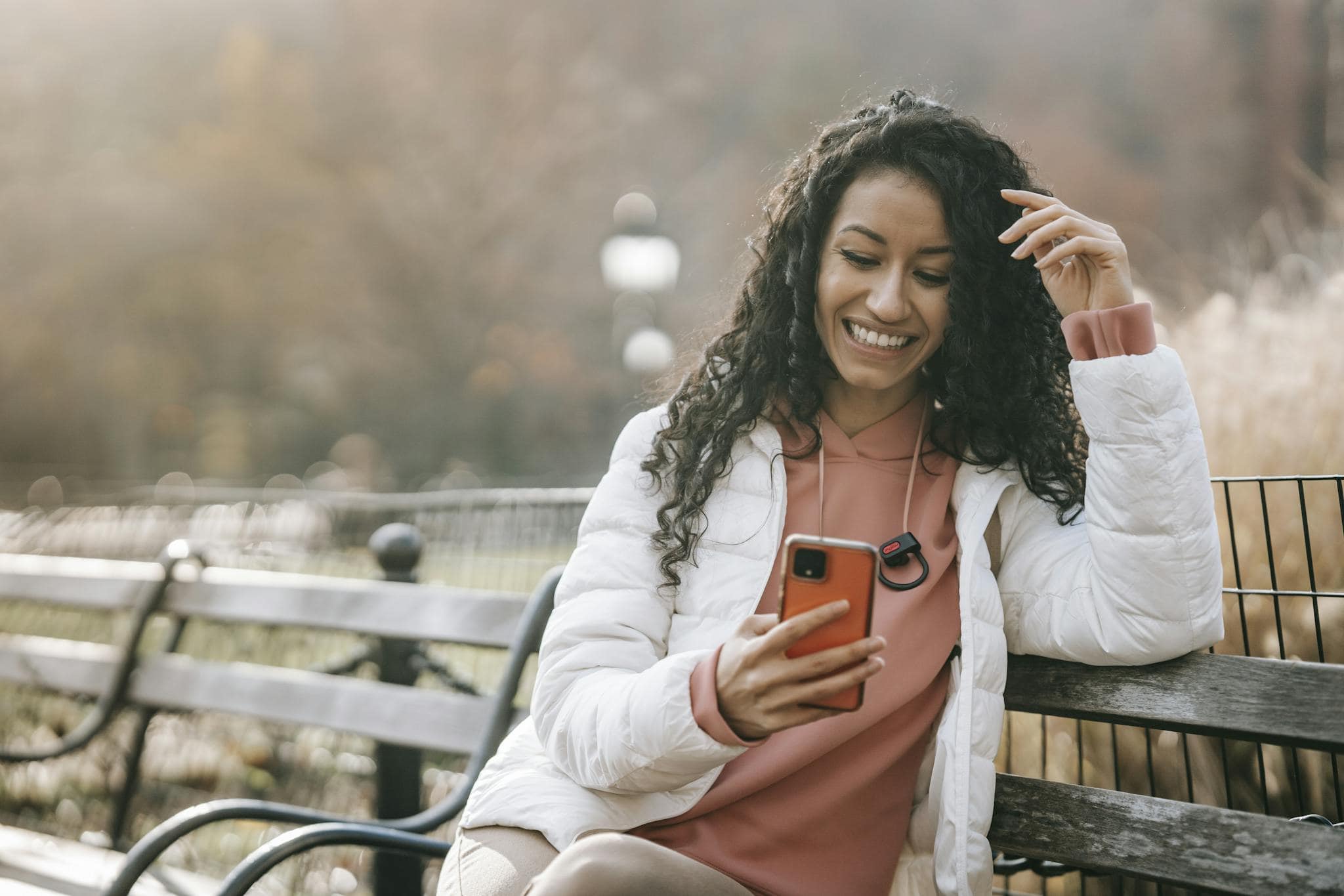 A cheerful woman enjoying a sunny autumn day, sitting on a bench and browsing her smartphone in the park.