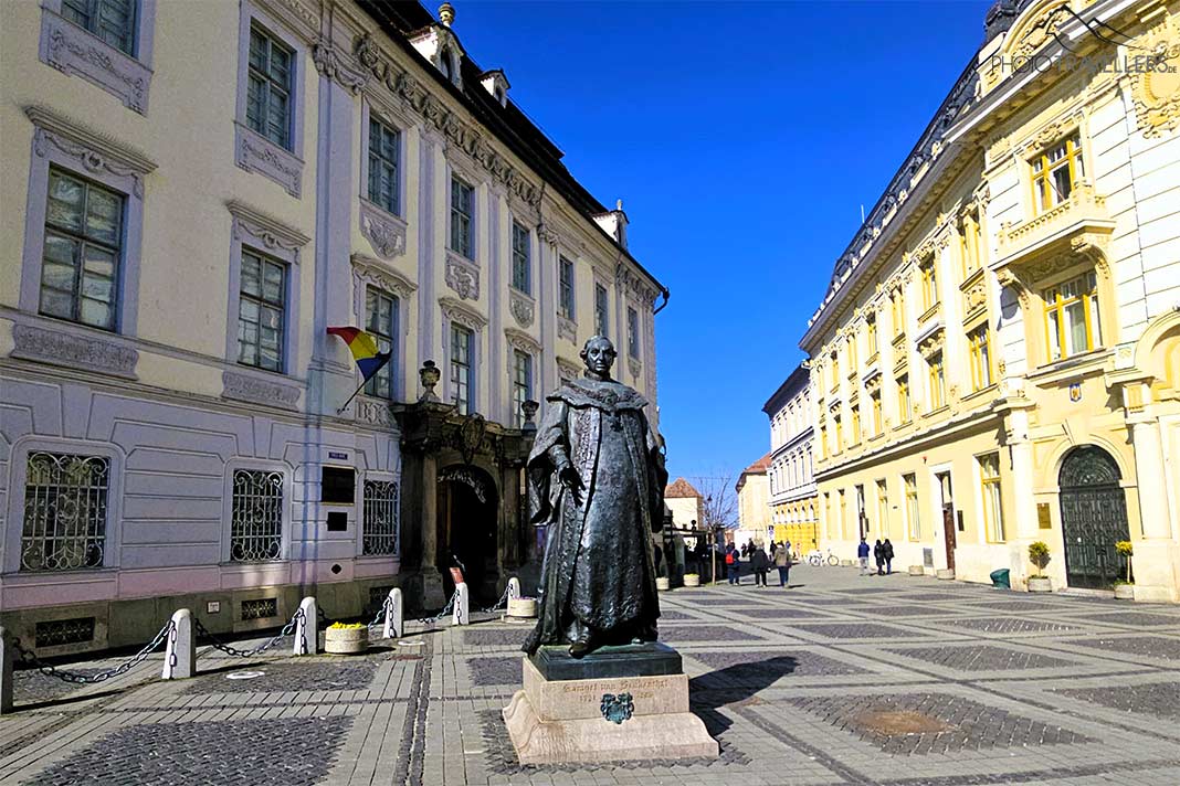 Die Bronzestatue von Baron Brukenthal steht direkt vor dem gleichnamigen Barock-Palais mit der weißen Fassade