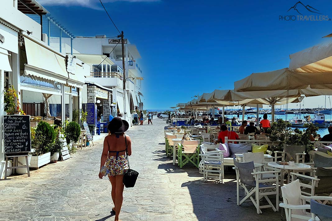 Eine Frau mit Hut und Rock spaziert entlang der Hafenpromenade von Aliki