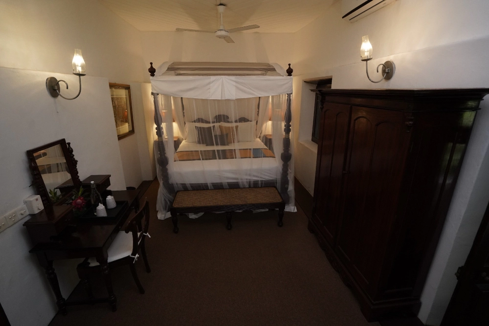 The Connelian room in Adigar's Manor, featuring a stylish canopy bed and a table, exuding a warm atmosphere.