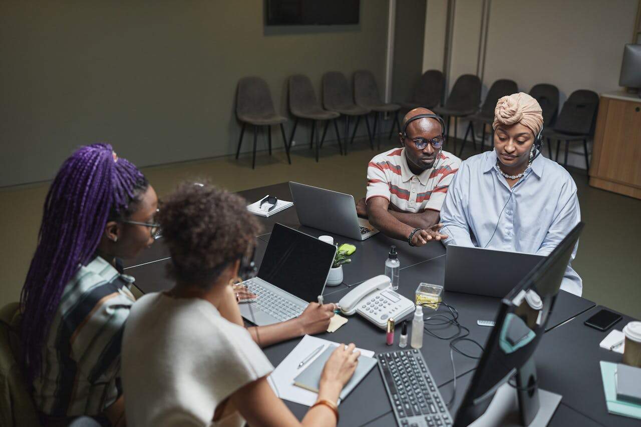 group-of-people-sitting-on-chair-7689855 A focused team working with laptops and documents at an office table, demonstrating teamwork and diversity.