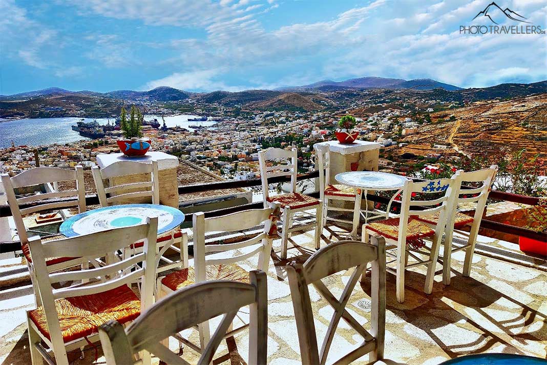 Leere Holztische- und Stühle auf einer Terrasse mit Blick auf den Hafen von Ermoupoli