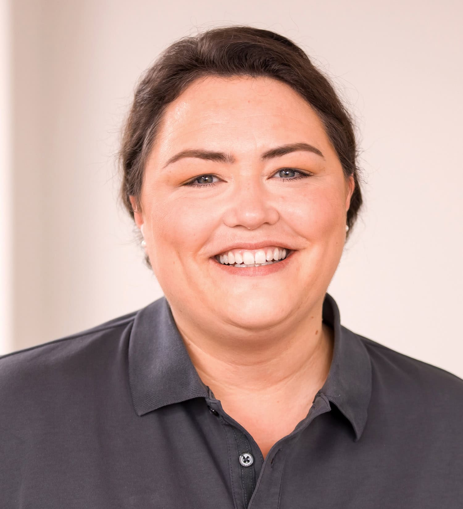 Eine Krankenschwester mit zurückgebundenen Haaren und grauem Poloshirt.