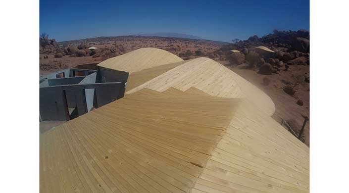 Mehrere große Holzbretter in geometrischen Mustern liegen in einer trockenen Landschaft unter klarem blauem Himmel.