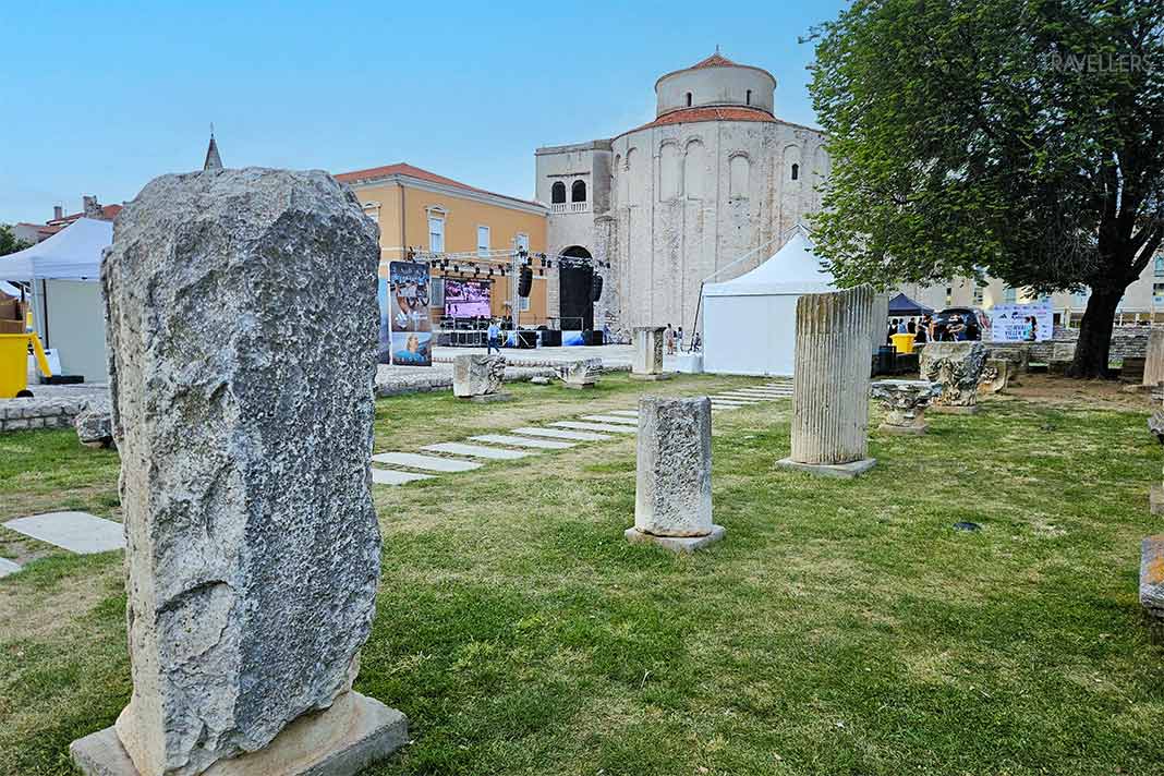 Stelen aus Stein sind auf dem Rasen vor der Donatuskirche aufgereiht