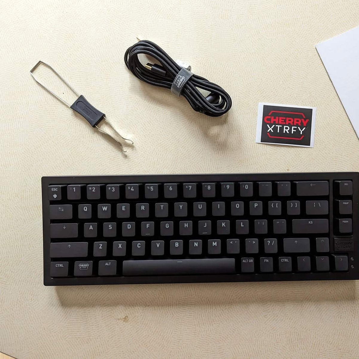 Clavier mécanique Cherry XTRFY K5V2 avec câble USB, clé de nettoyage, stickers et notice de démarrage, idéal pour gaming et bureautique, compatible avec PC et Mac.