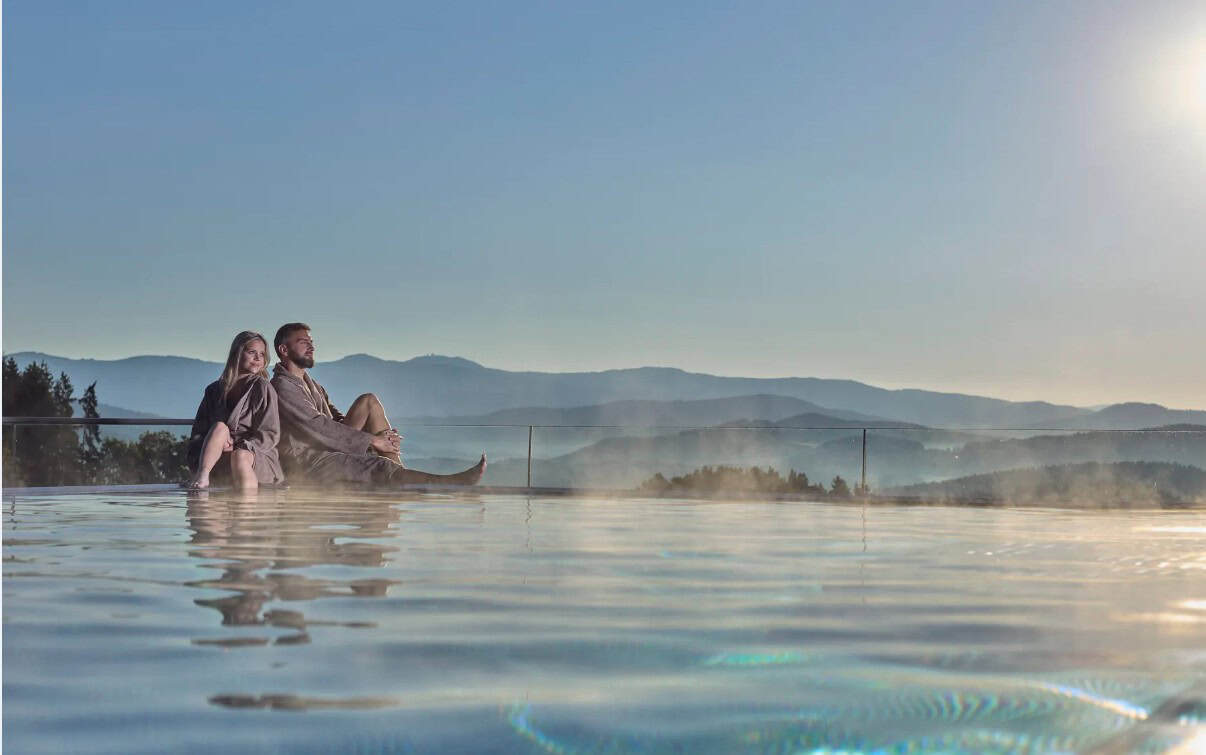 ein Paar sitzt am Rand des Aussenpool unseres Wellnesshotel und genießt die Wintersonne