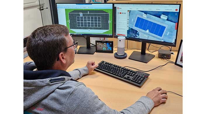 Person arbeitet am Computer mit zwei Monitoren, einer zeigt eine technische Zeichnung, der andere eine E-Mail-Anwendung. Ein weiteres Gerät steht auf dem Tisch.
