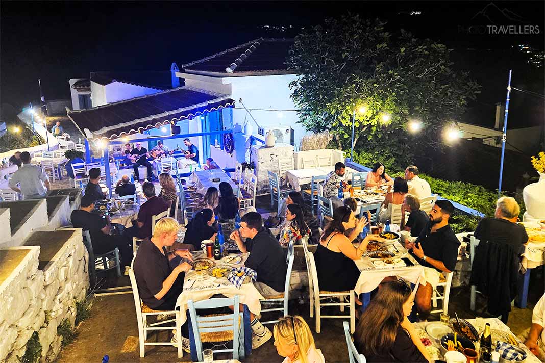 Viele Menschen sitzen nachts an den Tischen der Taverne Anatoli auf inmitten der Ruinen der Chora von Skopelos
