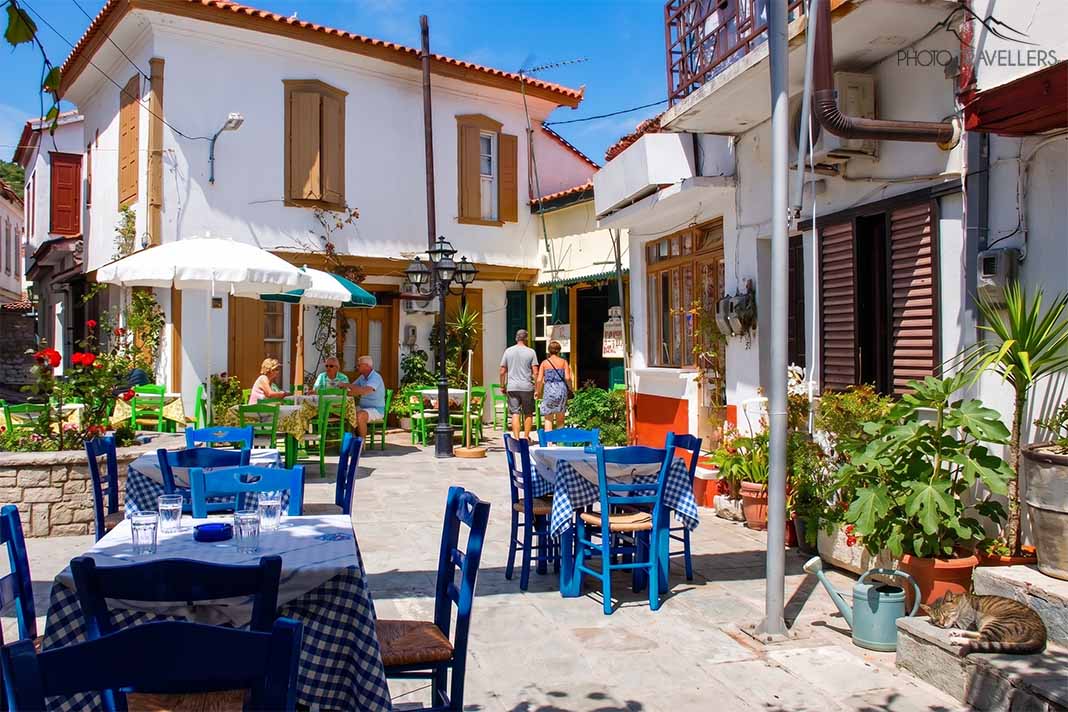 Einige Menschen sitzen und stehen an einer Taverne am Dorfplatz von Vourliotes