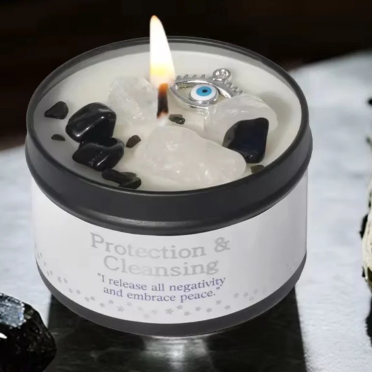 The Peace & Protection - White Sage & Frankincense Candle, adorned with black and white crystals and an evil eye charm, sits beside White Sage and a black stone—ideal for rituals promoting peace and protection.