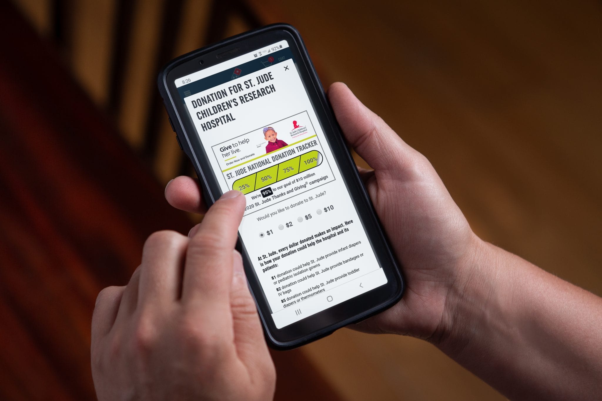 Hand using Domino’s mobile app to donate to St. Jude Children’s Research Hospital, showing donation tracker and options.