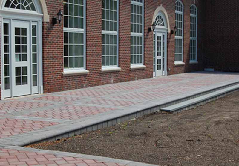 Brick ramp leading to a building with white doors and multiple large windows, demonstrating accessibility.