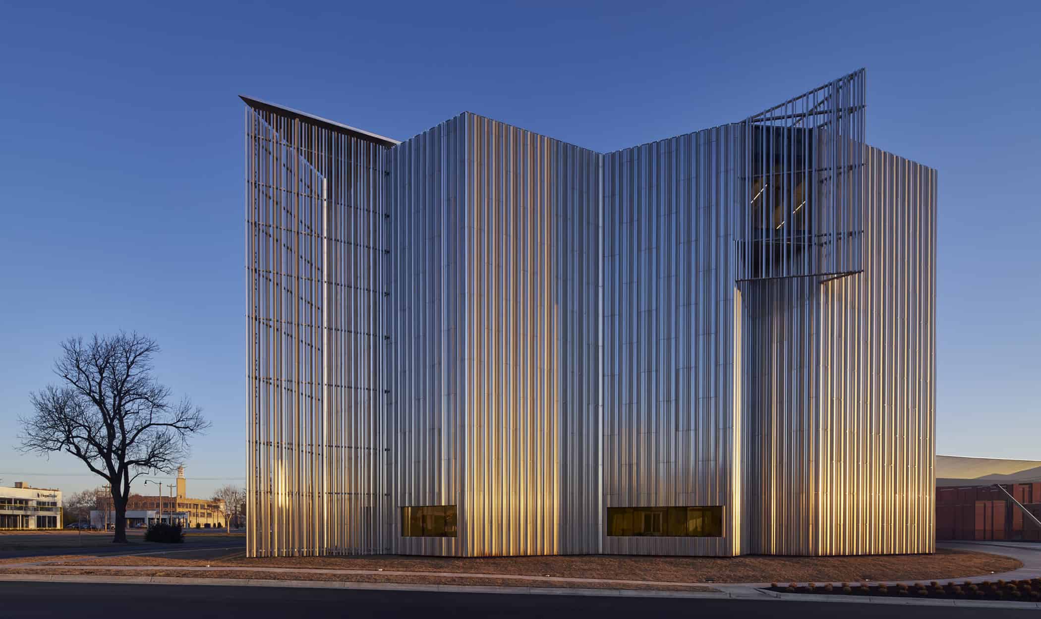Exterior of the Oklahoma Contemporary Arts Center during golden hour, showcasing the reflective aluminum fin façade and modern architectural design.