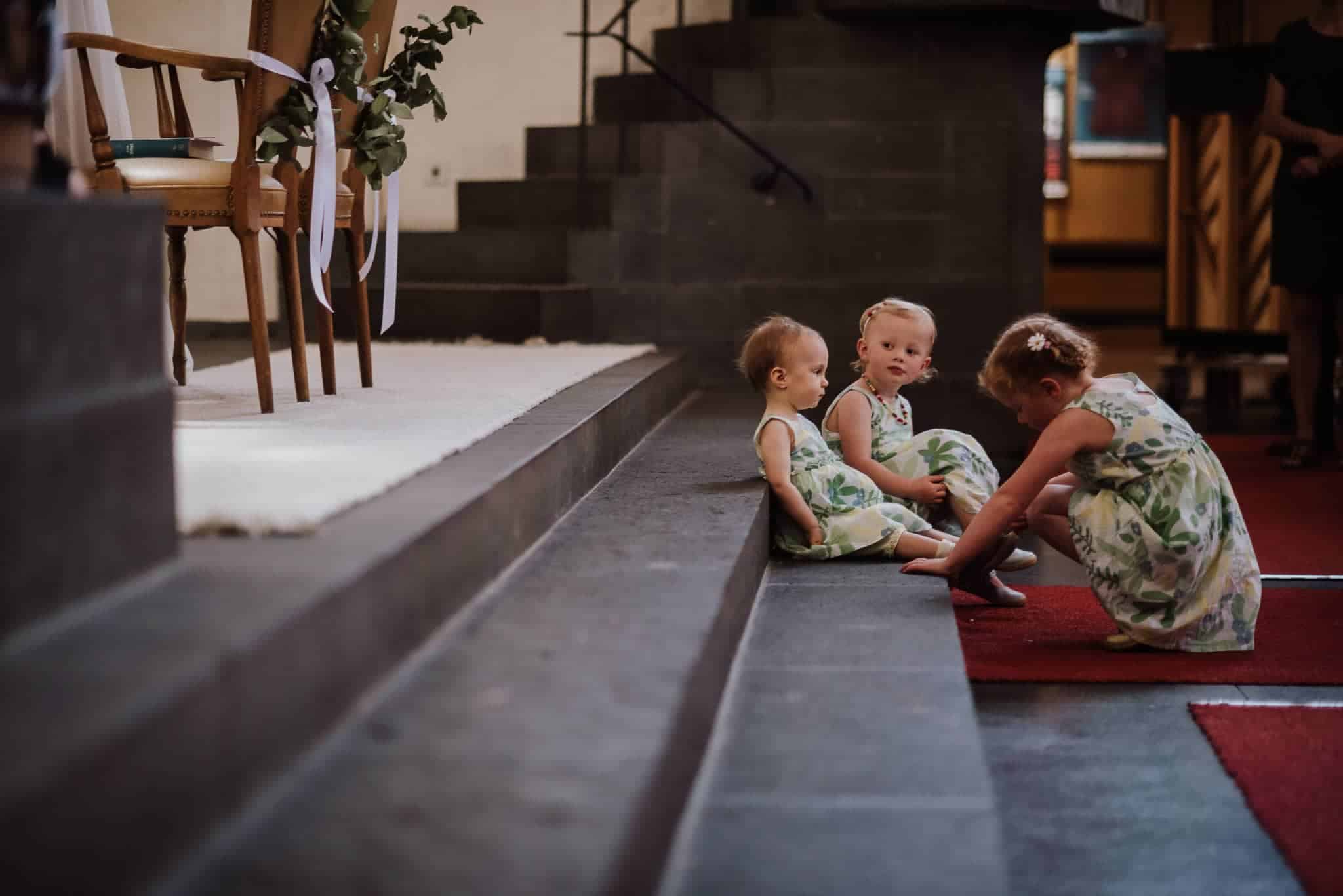 Drei Kinder in Blumenkleidern sitzen lachend auf den Stufen bei einer standesamtlichen Trauung auf Gut Hohenholz.