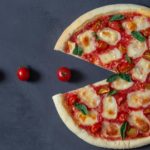 Tranches de pizza Margherita avec tomates cerises, mozzarella, et basilic frais, sur une surface noire élégante.