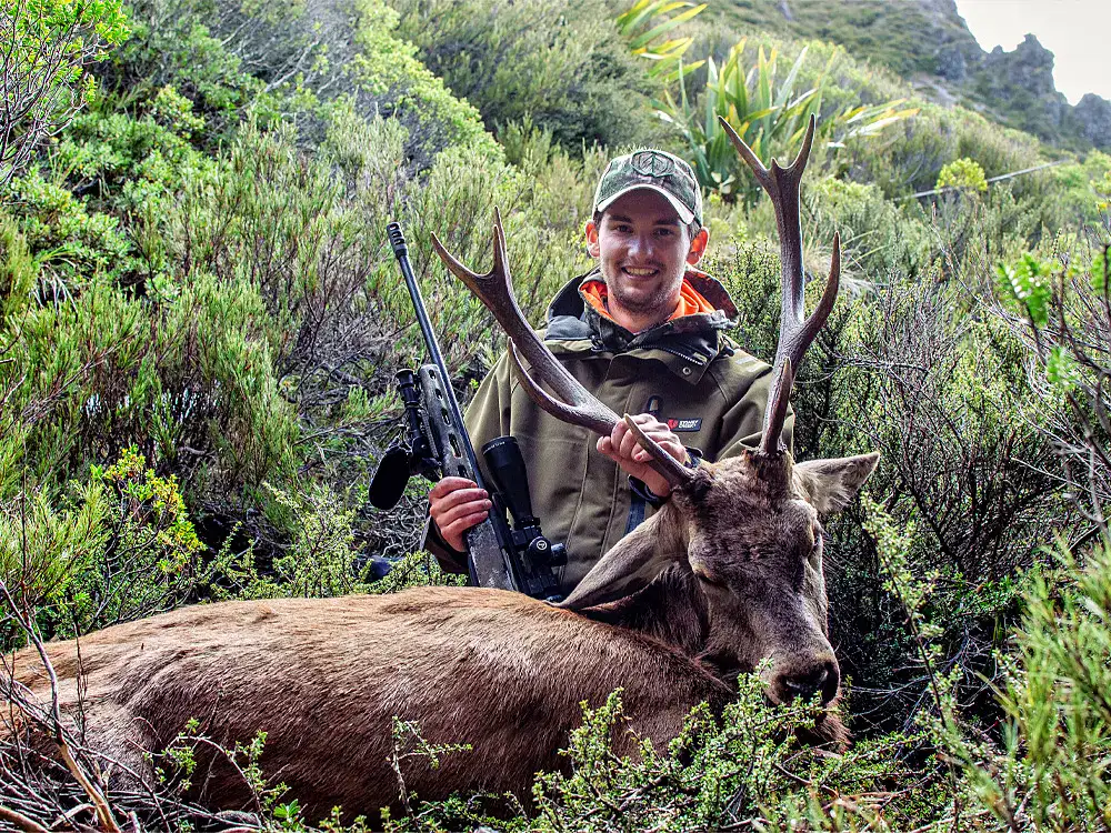 Hirschjagd im Bergrevier – präzises Setup mit Repetierer Junge Jäger mit erlegtem Hirsch im Gebirge – erfolgreiche Hirschjagd mit Repetierer und Zielfernrohr
