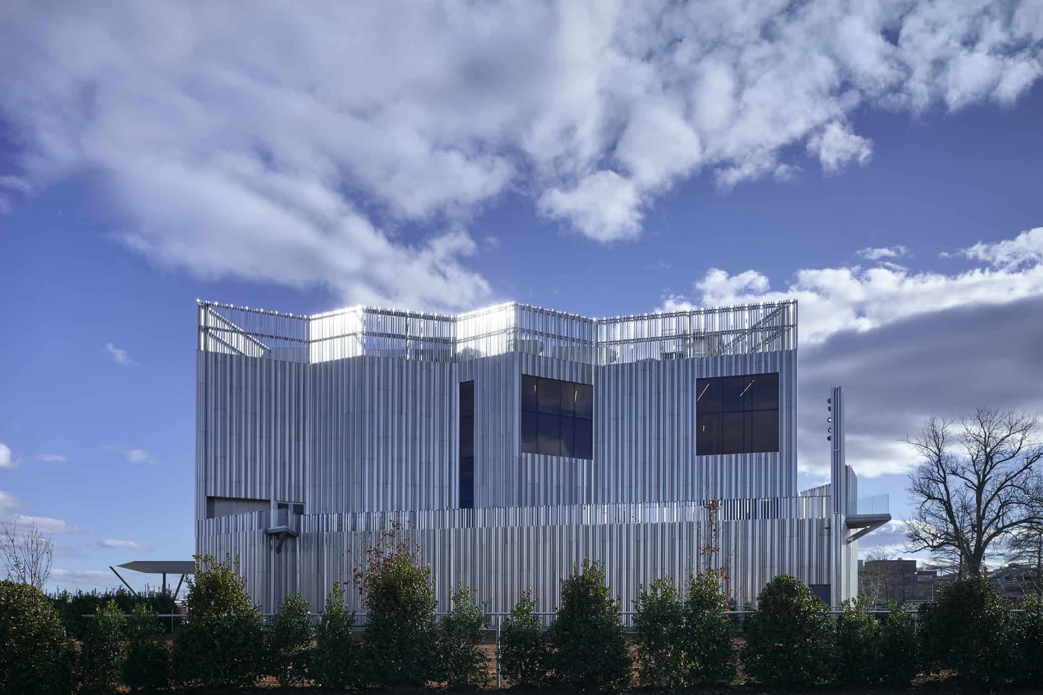 Daytime side view of the Oklahoma Contemporary Arts Center, showcasing its layered aluminum façade with vertical fins and reflective surfaces beneath a bright sky.