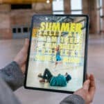 Ein Foto eines Tablets, das von einer Person gehalten wird. Auf dem Tablet ist eine Modewerbung innerhalb der Halle.