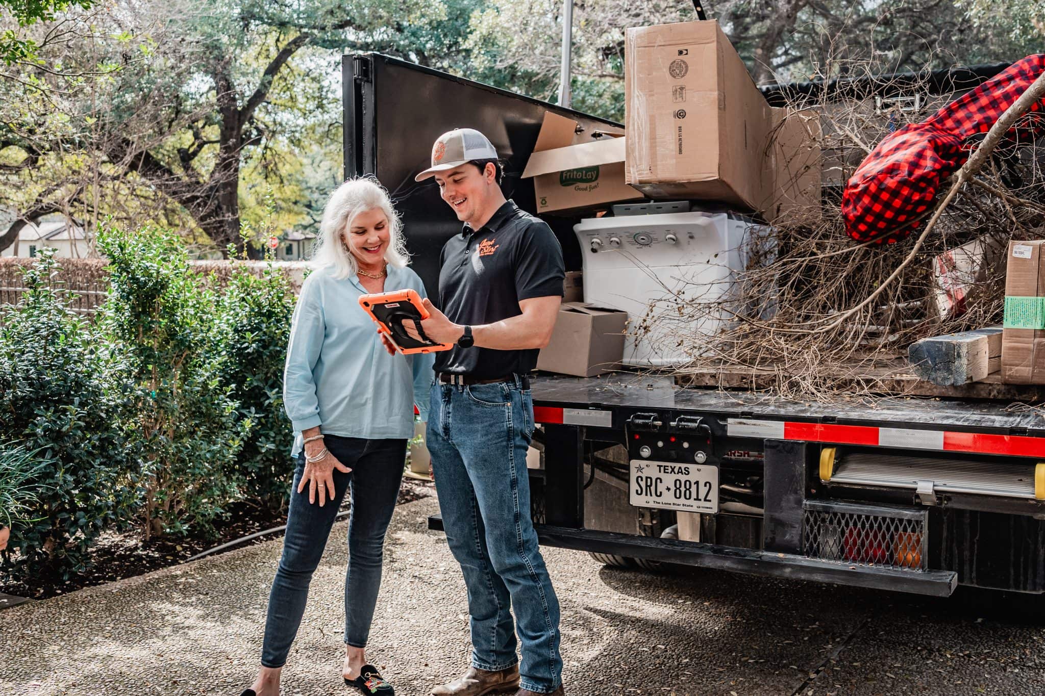JunkStart team member showing a customer transparent pricing on a tablet beside a loaded junk removal truck in San Antonio, Texas.