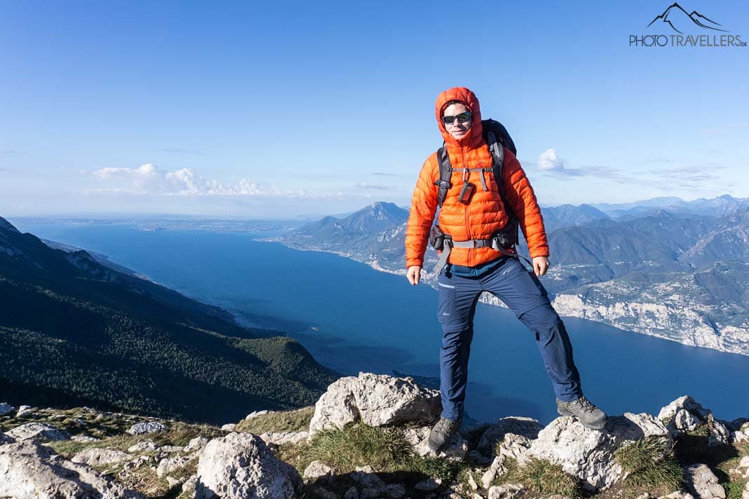 Reisejournalist Florian Westermann in einer orangen Daunenjake auf dem Monte Baldo mit Blick auf den Gardasee