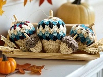 Crocheted acorns in blue, cream, and brown rest on straw in a tray, with pumpkins and leaves on a white mantel. Free crochet pattern