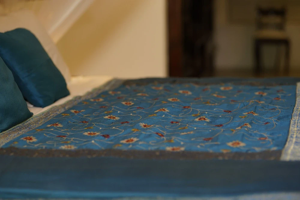 A bed adorned with blue pillows and a blue blanket in the Peacock Royal room of Adigar's manor.