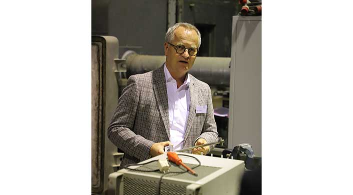 Bild von Rigo Giese vom Institut für Ziegelforschung Ein Mann mit Brille und kariertem Sakko hält technische Geräte in den Händen und steht in einem industriellen Umfeld.