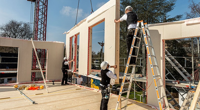 Bauarbeiter mit Helm richtet eine große Wand mit Fensteröffnung auf einer Baustelle aus.
