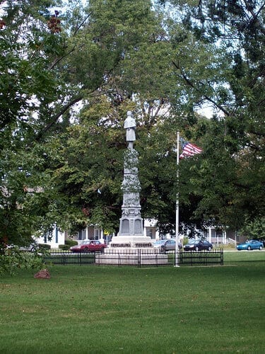 Historic Civil War soldier monument in a city park surrounded by trees and American flag.