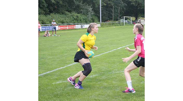 Eine Frau im gelben Trikot spielt Rugby auf einem grünen Spielfeld und hält den Ball, während sie läuft.