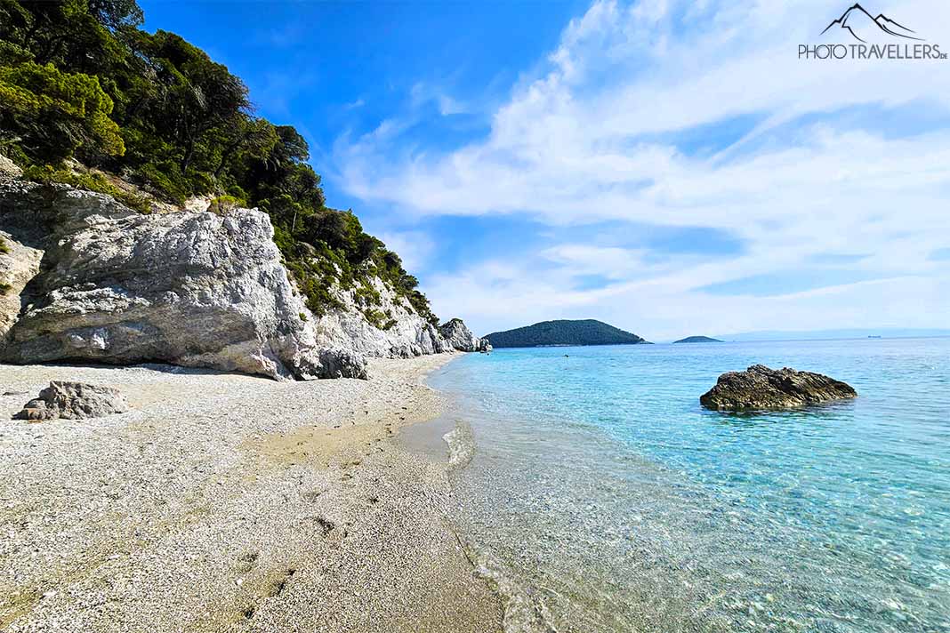 Begrünte Steilfelsen am Sandkiesstrand Hovolo mit türkisfarbenem Wasser und Felsen