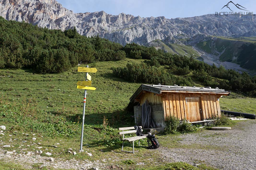 Eine kleine Holzhütte vor den Bergen, davor ein Wegweiser