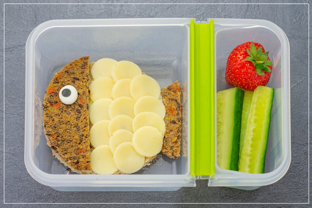 Gesundes Pausenbrot für Kinder in lustiger Tierform als Kugelfisch-Käsebrot mit Gurkensticks und Erdbeere